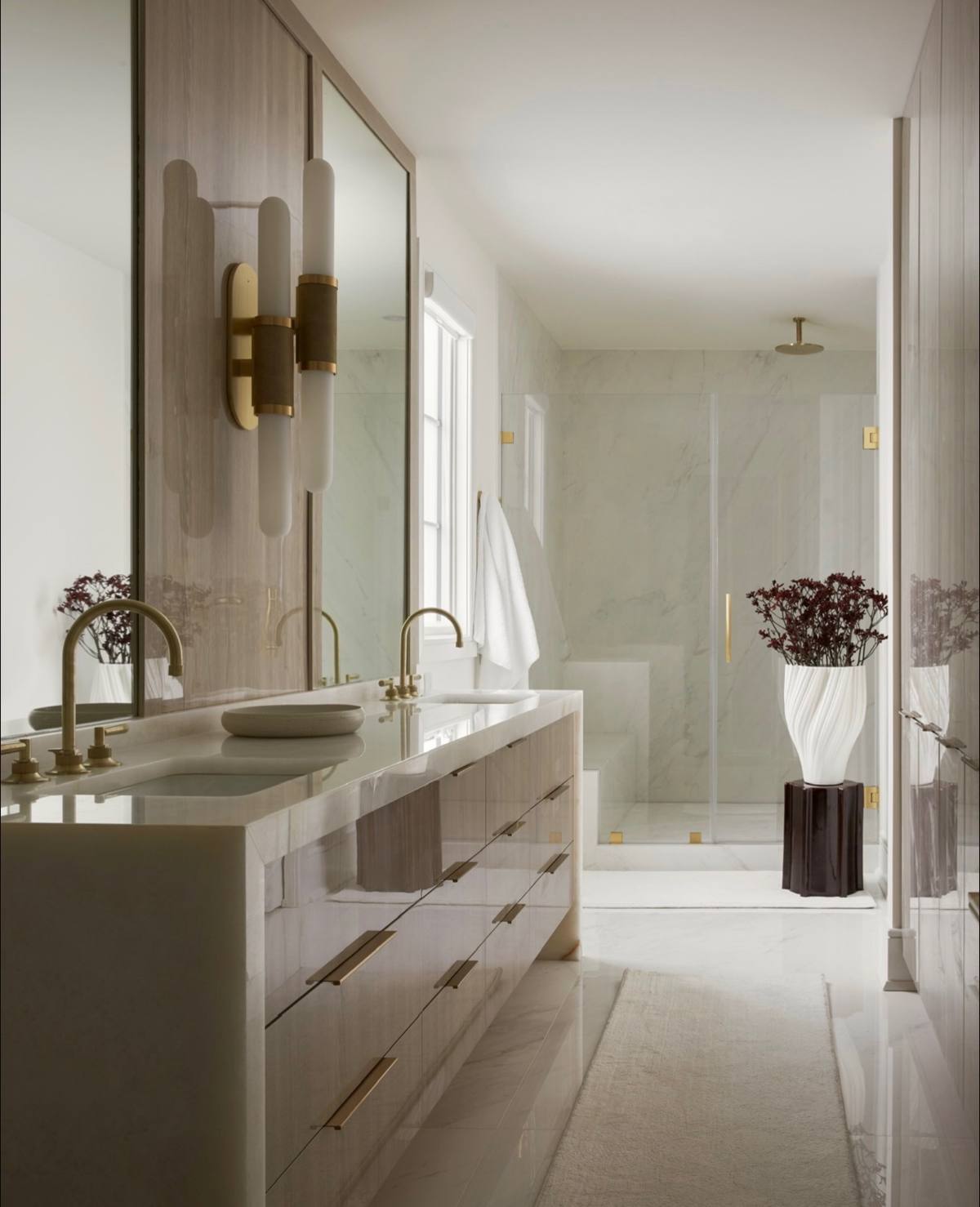 Primary bath with double vanity, brass fixtures, and a fluted vase of stems