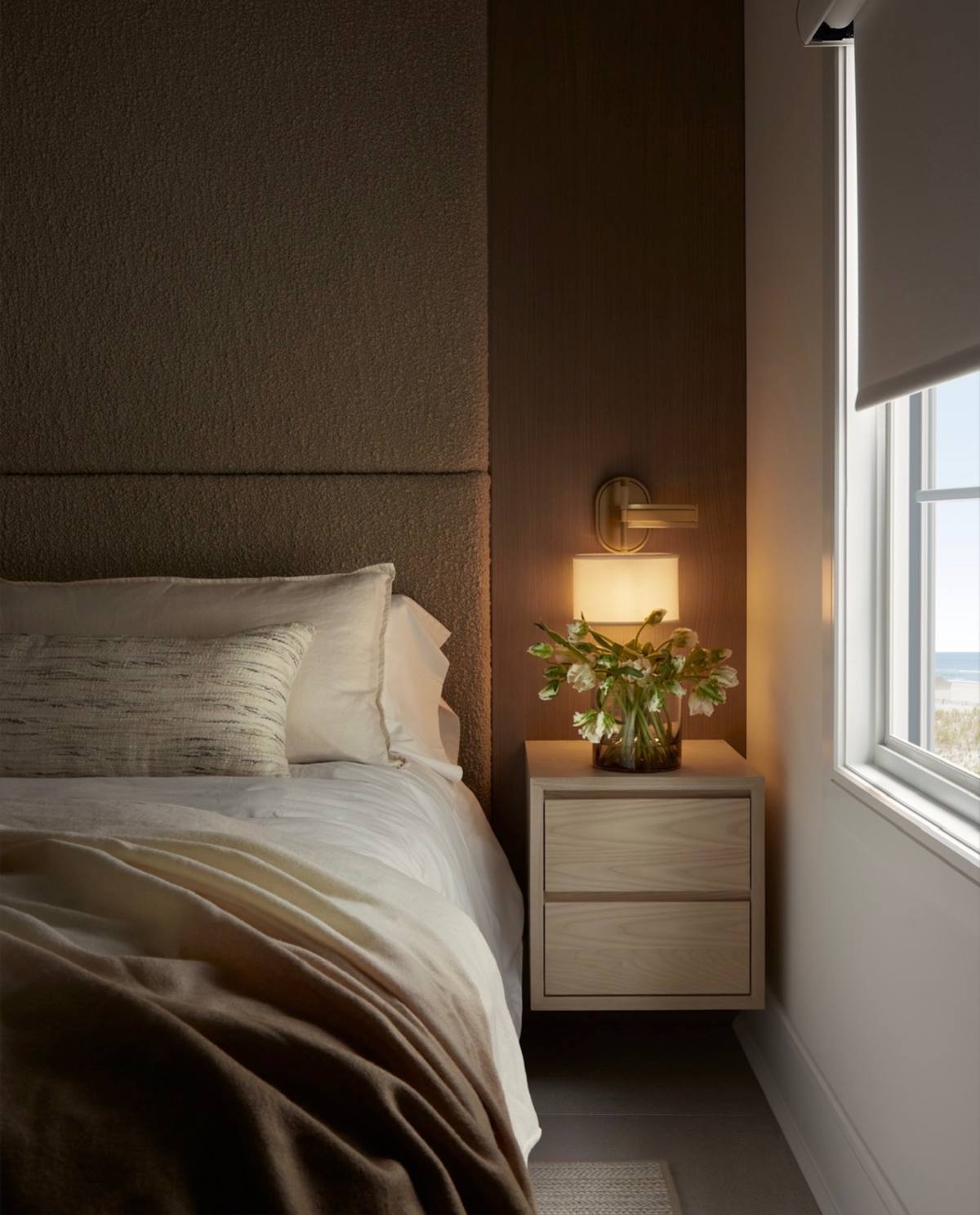 Bedroom at dusk with warm lamplight and greenery on the nightstand