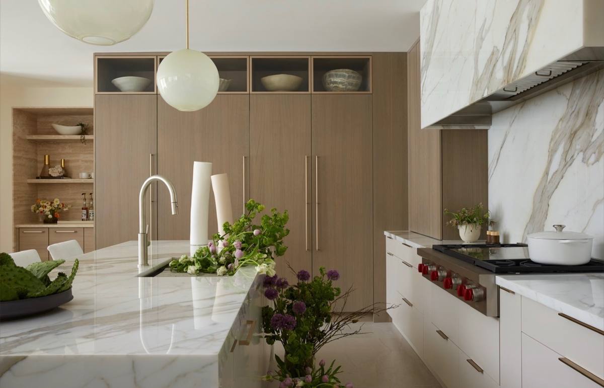 Kitchen with marble waterfall island and oak cabinetry, styled with greenery and ceramic vessels