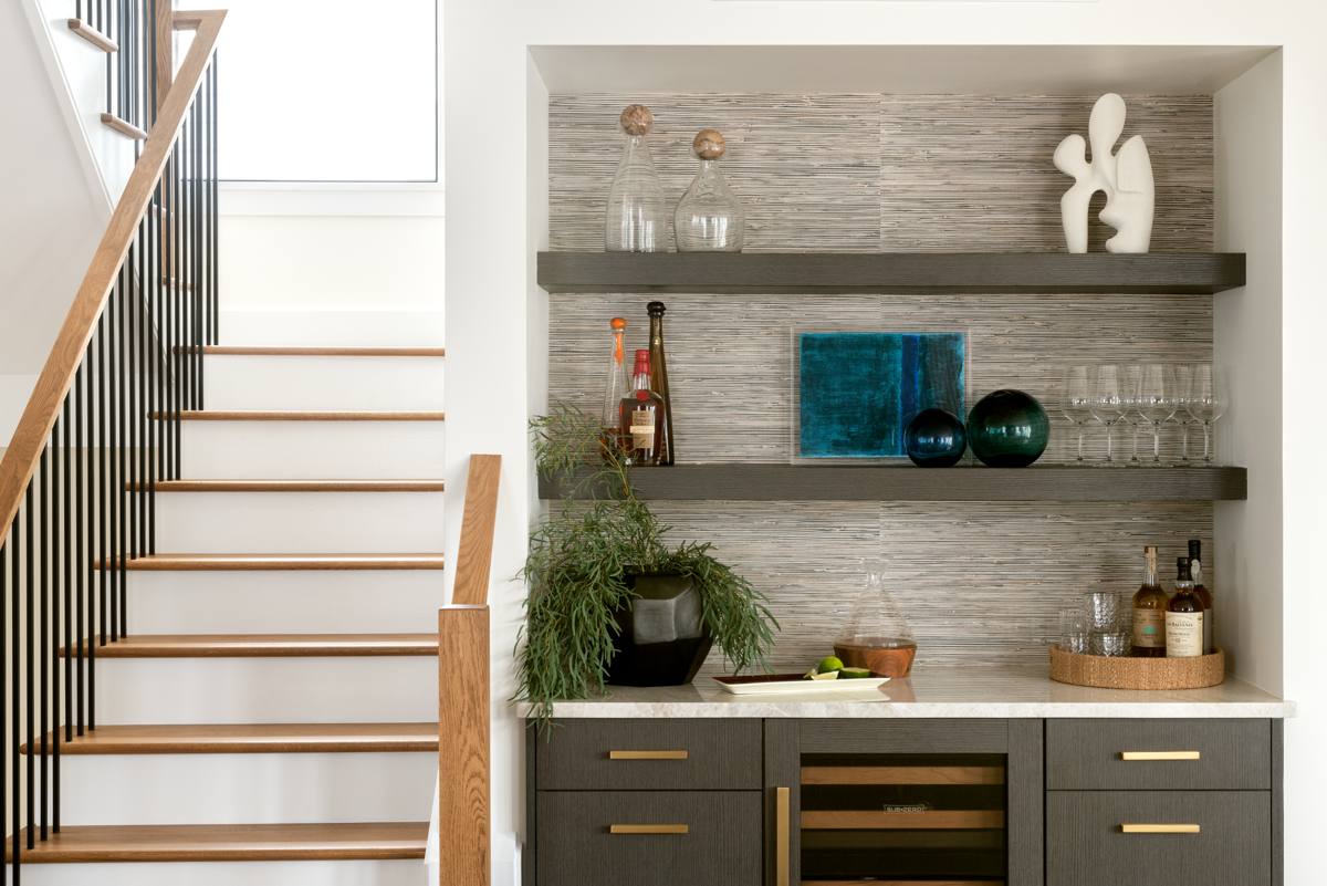 Built-in bar with grasscloth backing, floating shelves, sculpture, and teal glass
